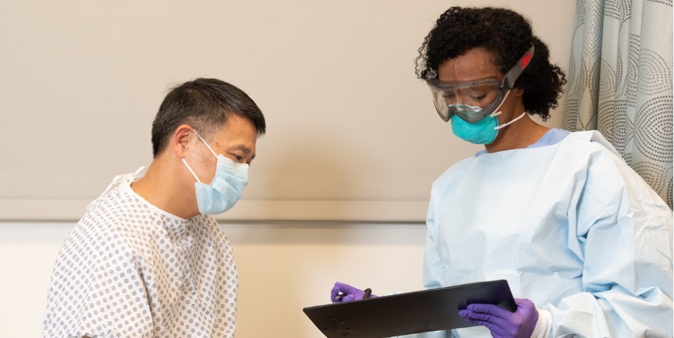 health care worker in a protective respirator and goggles conversing with patient